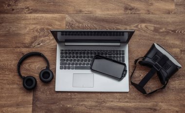 Modern aletlerin düz kompozisyonu. Laptop, vr kask, kulaklık, ahşap arka planda akıllı telefon. Üst görünüm
