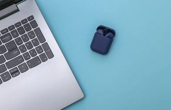 Laptop and wireless headphones with charger case on blue background. Top view