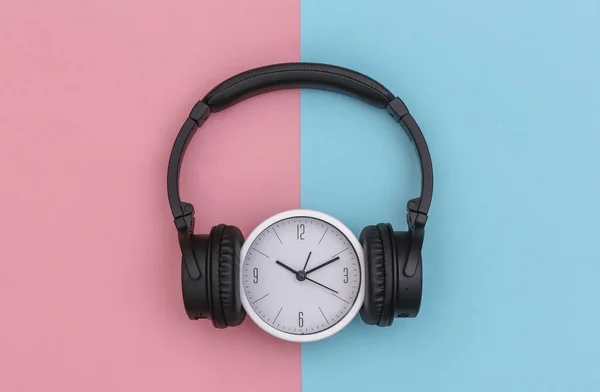 带有黑色立体声耳机的白色钟表 背景为粉红色的蓝色粉底 顶部视图 — 图库照片