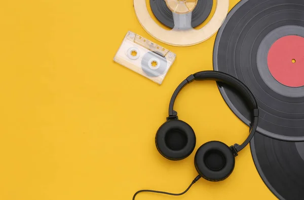 Retro vinyl records, audio magnetic reel, audio cassette and stereo headphones on yellow background. Copy space. Top view