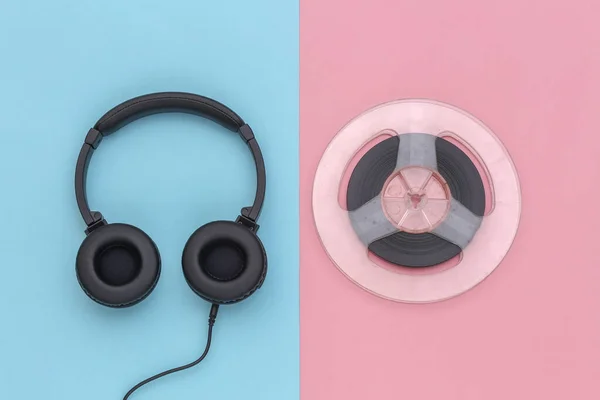 Stereo headphones and magnetic audio reel on pink blue pastel background. Top view
