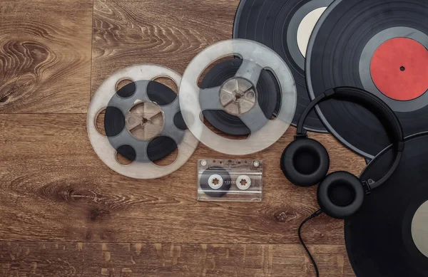 Retro vinyl records, audio magnetic reel, audio cassette and stereo headphones on wooden background. Top view