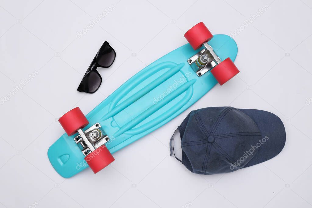 Flat lay composition of mini cruiser board, sunglasses and cap on white background. Youth, hipster accessories. Top view