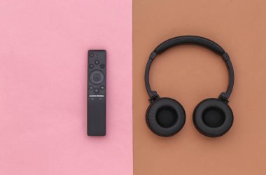 Stereo kablosuz kulaklık ve kahverengi-pembe arka planda televizyon kumandası. Üst görünüm
