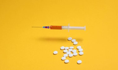 Tıbbi minimalist konsept. Şırınga, sarı arka planda haplar.