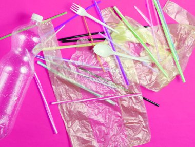 Plastiksiz. Deniz ve okyanusların plastik kirliliği kavramı. Selofan çanta, plastik şişe, tek kullanımlık çatal ve kaşıklar, pembe sarı arka planda kokteyl tüpleri..