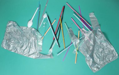 Kirlilik ortamı kavramı. Selofan çanta, plastik şişe, tek kullanımlık çatal ve kaşıklar, mavi arka planda kokteyl tüpleri. Üst görünüm