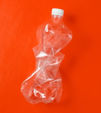 Minimalist ekolojik kavram. Turuncu arka planda buruşmuş plastik şişe. Çevresel plastik kirliliği