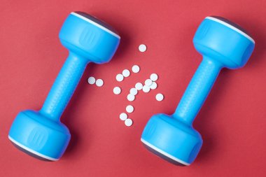 Spor Eczanesi. Plastik halterler, kırmızı arka planda haplar. Üst görünüm.