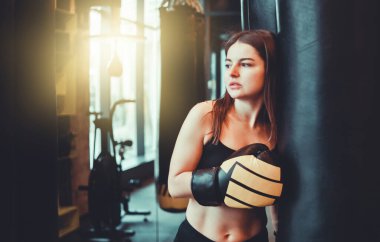 Boks eldivenli yorgun genç bir kadın boks antrenmanından sonra kum torbasıyla dinleniyor..