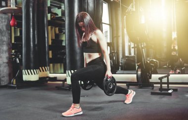 Spor salonunda antrenman bacakları. Çekici fit kadın bardan disklerle hamle yapıyor..