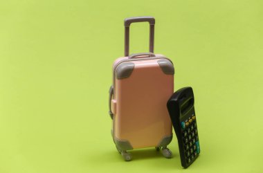 Seyahat masrafları. Yeşil arka planda hesap makinesi olan mini plastik bir valiz. Asgari biçim