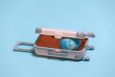 Seyahat ya da seyahat konsepti. Mavi arka planda küre olan mini plastik bir valiz..