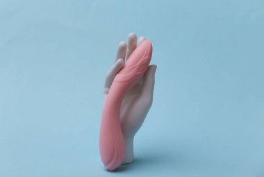 White mannequin hand holds dildo on blue background. Sex toy