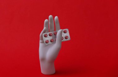 Beyaz manken elinde kırmızı arka planda hapların kabarcıkları var.