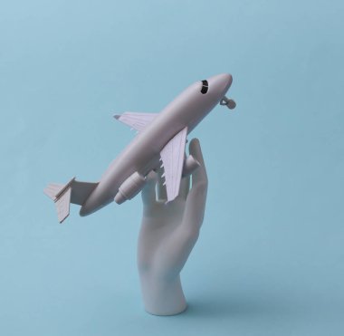 Beyaz bir manken elinde mavi arka planda küçük bir uçak tutuyor. Seyahat, uçuş konsepti