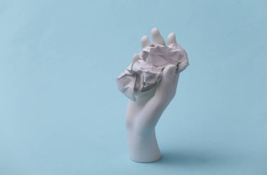 Beyaz manken el, mavi arka planda buruşmuş kağıt topları tutuyor.