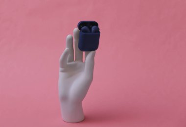 Beyaz manken elinde pembe arka planda şarj kutusu olan kablosuz kulaklık.