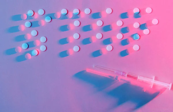 Stop the drugs. Lettering stop with pills. The concept of addiction. Syringe and pills, neon red-blue lighting. Top view