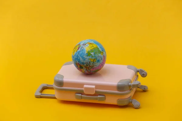 International travel concept. Mini pink plastic travel suitcase on yellow background. Minimal style