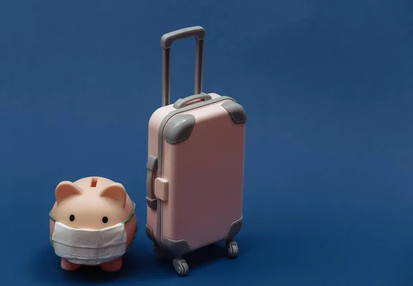 在Covid 19旅行 经典蓝色背景的小型塑料旅行箱和带面罩的储蓄罐 — 图库照片