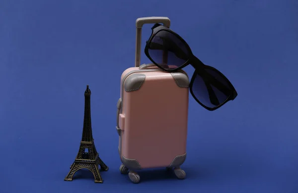 Traveled to Paris. Mini plastic travel suitcase with sunglasses and statuette of the Eiffel Tower on classic blue background.