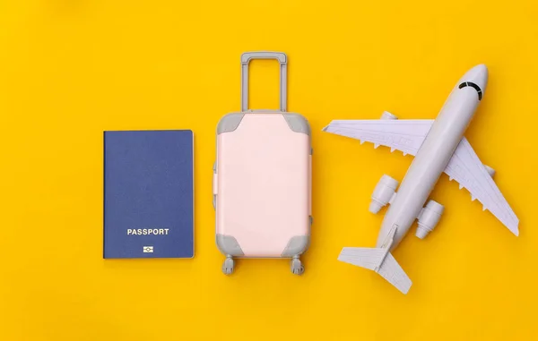 Travel flat lay. Mini plastic travel suitcase, air plane and passport on yellow background. Minimal style. Top view