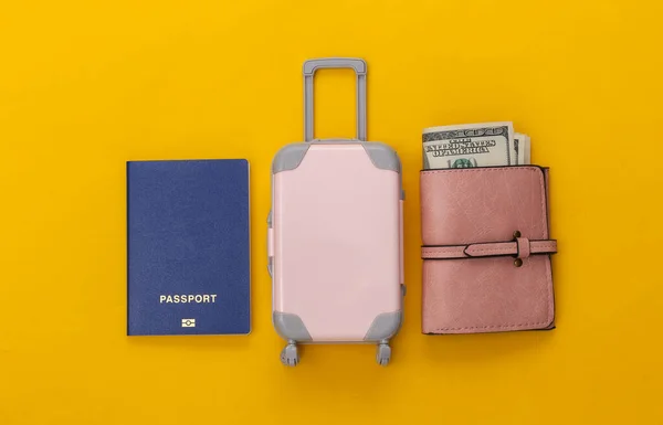 Travel flat lay. Mini plastic travel suitcase, purse and passport on yellow background. Minimal style. Top view