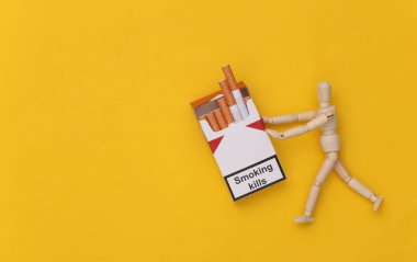 Kukla sarı arka planda bir paket sigara tutuyor. Sigara bağımlılığı. Sigara öldürür.