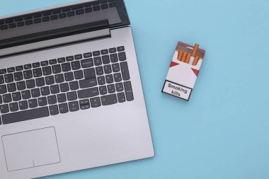 Laptop ve bir paket sigara mavi arka planda. Üst görünüm