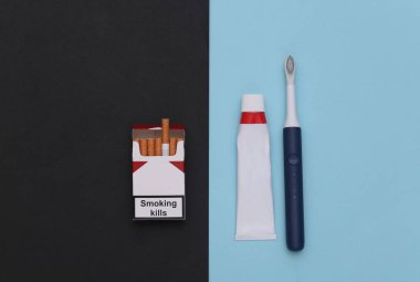 Diş bakımı ve kötü alışkanlıklar kavramı. Bir paket sigara, mavi siyah arka planda diş fırçası olan bir tüp diş macunu.