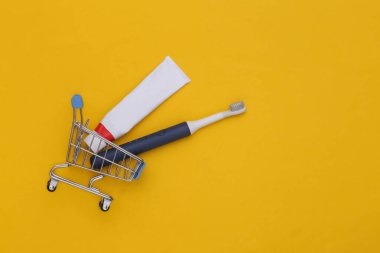 Diş bakımı. Sarı arka planda diş macunu ve diş fırçasıyla alışveriş arabası. Üst görünüm
