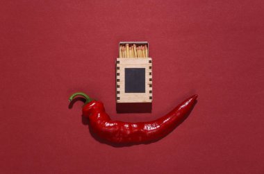 Kırmızı arka planda baharatlı kırmızı biber ve kibrit.