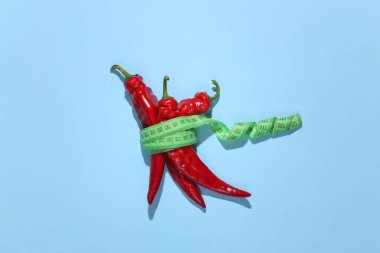 Kırmızı biberler mavi arka planda bir mezura ile sarılmış. Diyet kavramı