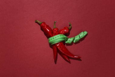 Kırmızı arka planda kırmızı biber şeridine sarılı kırmızı biber. Diyet kavramı