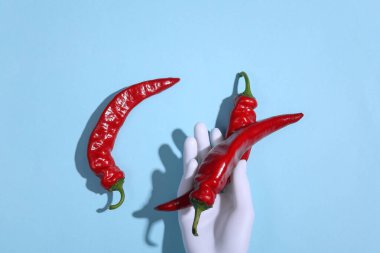 Mavi arka planda acı biber tutan manken eli