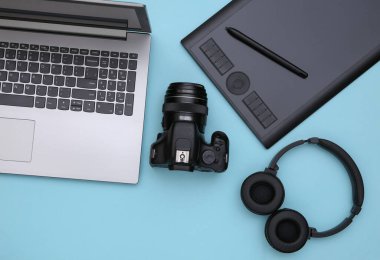 Bir fotoğrafçının ya da rötuşçunun çalışma alanı. Laptop, grafik tablet, kamera ve kulaklıklar mavi arka planda. Üst Manzara. Düz yatıyordu