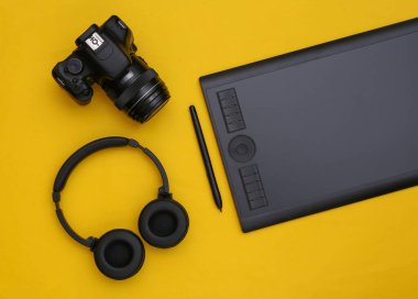 Sarı arka planda kalem, kulaklık ve kamera olan grafiksel tablet. Üst görünüm