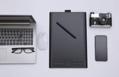 Fotoğrafçı ya da rötuşçu çalışma alanı. Laptop, grafik tablet, kamera ve kulaklıklar beyaz arkaplanda. Üst görünüm.