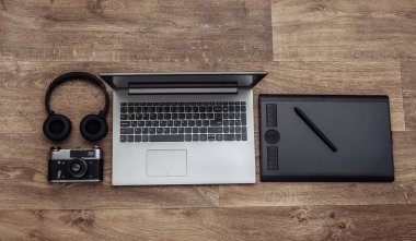 Bir fotoğrafçının ya da rötuşçunun çalışma alanı. Laptop, grafik tablet, kamera ve kulaklıklar ahşap arka planda. Üst görünüm
