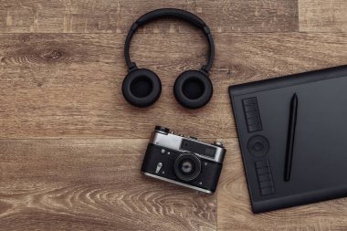 Ahşap zemin üzerinde kalem, kulaklık ve kamera olan grafiksel tablet. Üst görünüm