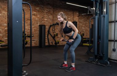 Spor salonunda kablo egzersiz makinesiyle mükemmel vücut eğitimi almış formda bir kadın.