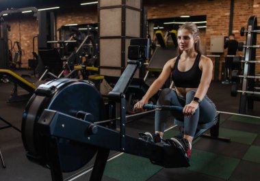 Athletic woman training on the rowing machine in gym clipart