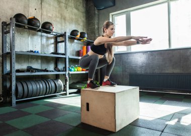 Genç bir kadın atlama egzersizi yapıyor. Formda bir kadın spor salonunda çömelme hareketi yapıyor. Çapraz eğitim