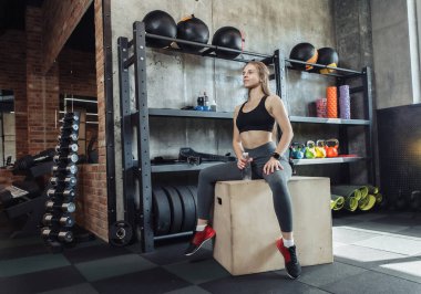 Genç beyaz kadın modern spor salonundaki ahşap bir spor salonunda dinleniyor.