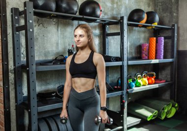 Mükemmel vücutlu sağlıklı bir kadın spor salonunda dambılları tutuyor.