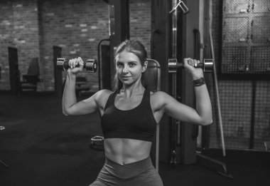 Genç, zayıf, formda bir kadın spor salonunda omuz kasları çalıştırıyor.