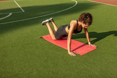 Neşeli sağlıklı kadın dışarıda yoga minderinde şınav egzersizi yapıyor.