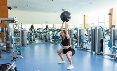 Genç sportif formda bir kadın modern bir hafif spor salonunda ilaç topuyla antrenman yapıyor. Çapraz eğitim