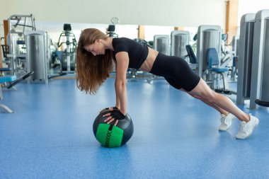 Genç sportif formda bir kadın modern ışık spor salonunda sağlık topuyla şınav çekiyor. Çapraz eğitim